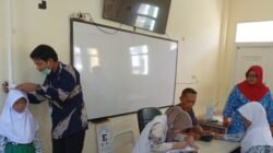 Seorang nakes memeriksa tekanan darah siswa sekolah dasar menggunakan tensimeter di ruang kelas