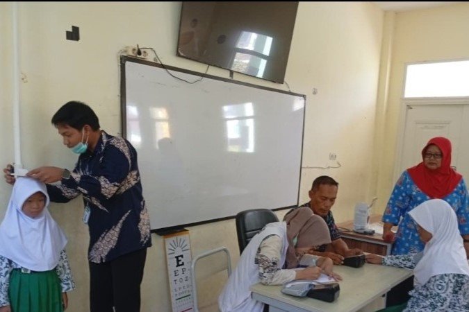 Seorang nakes memeriksa tekanan darah siswa sekolah dasar menggunakan tensimeter di ruang kelas