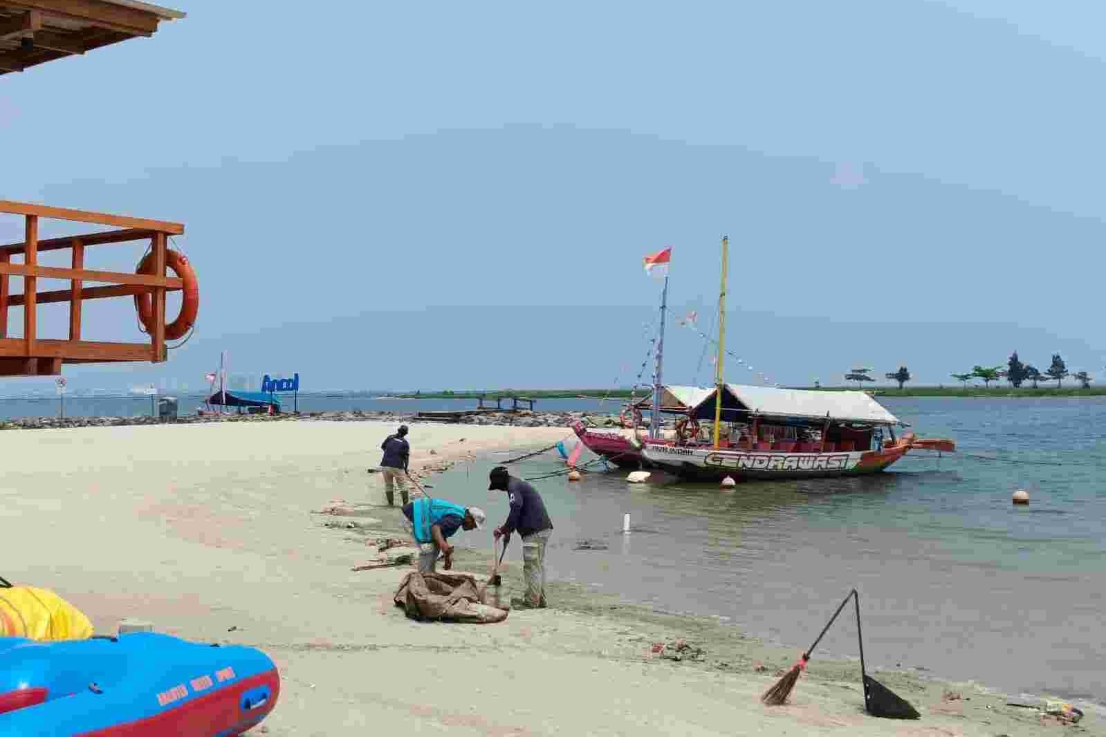Pekerja membersihkan pantai di dekat perahu tradisional di Pantai Ancol.
