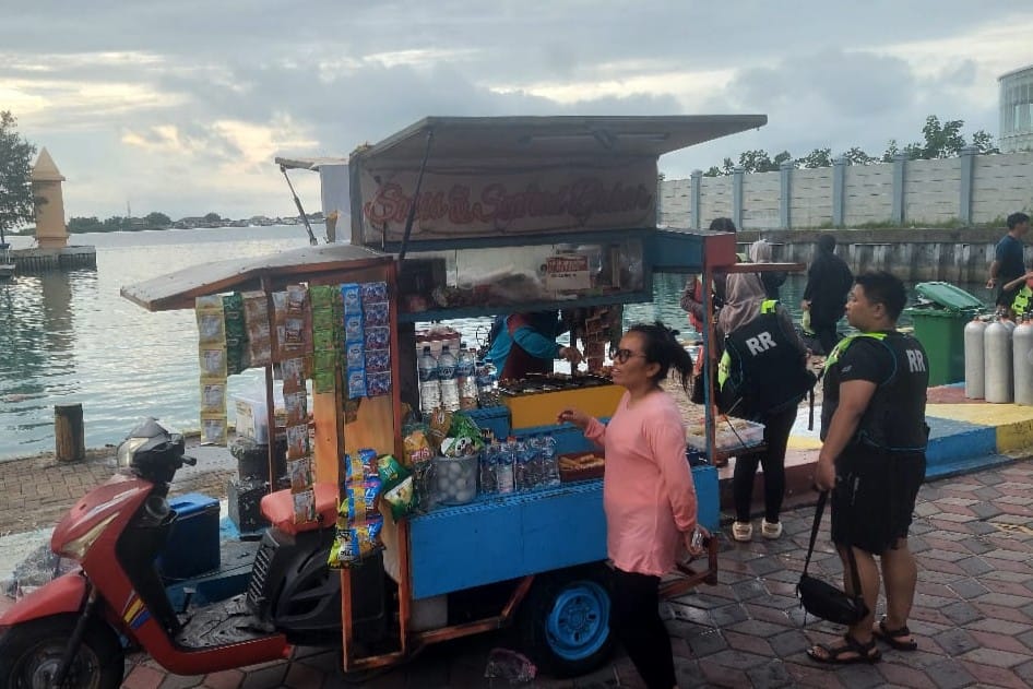 Pedagang jajanan di Pulau Pramuka menunggu pembeli di tepi pantai saat libur Lebaran, dengan gerobak penuh makanan dan minuman.