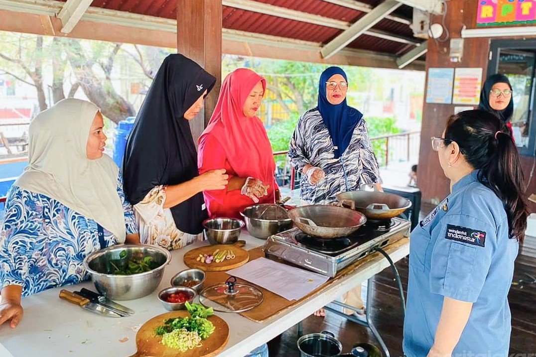 Warga dan ibu rumah tangga di Pulau Kelapa memegang spatula mengaduk masakan Ayam Bumbu Woku di wajan
