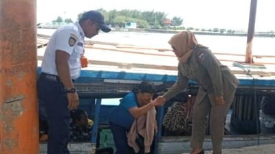 Personel Satpol PP Kepulauan Seribu membantu seorang penumpang lanjut usia turun dari kapal di dermaga.