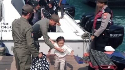 Personel Satpol PP Kepulauan Seribu membantu seorang anak turun dari kapal di dermaga dengan pengamanan bersama personel Polri.